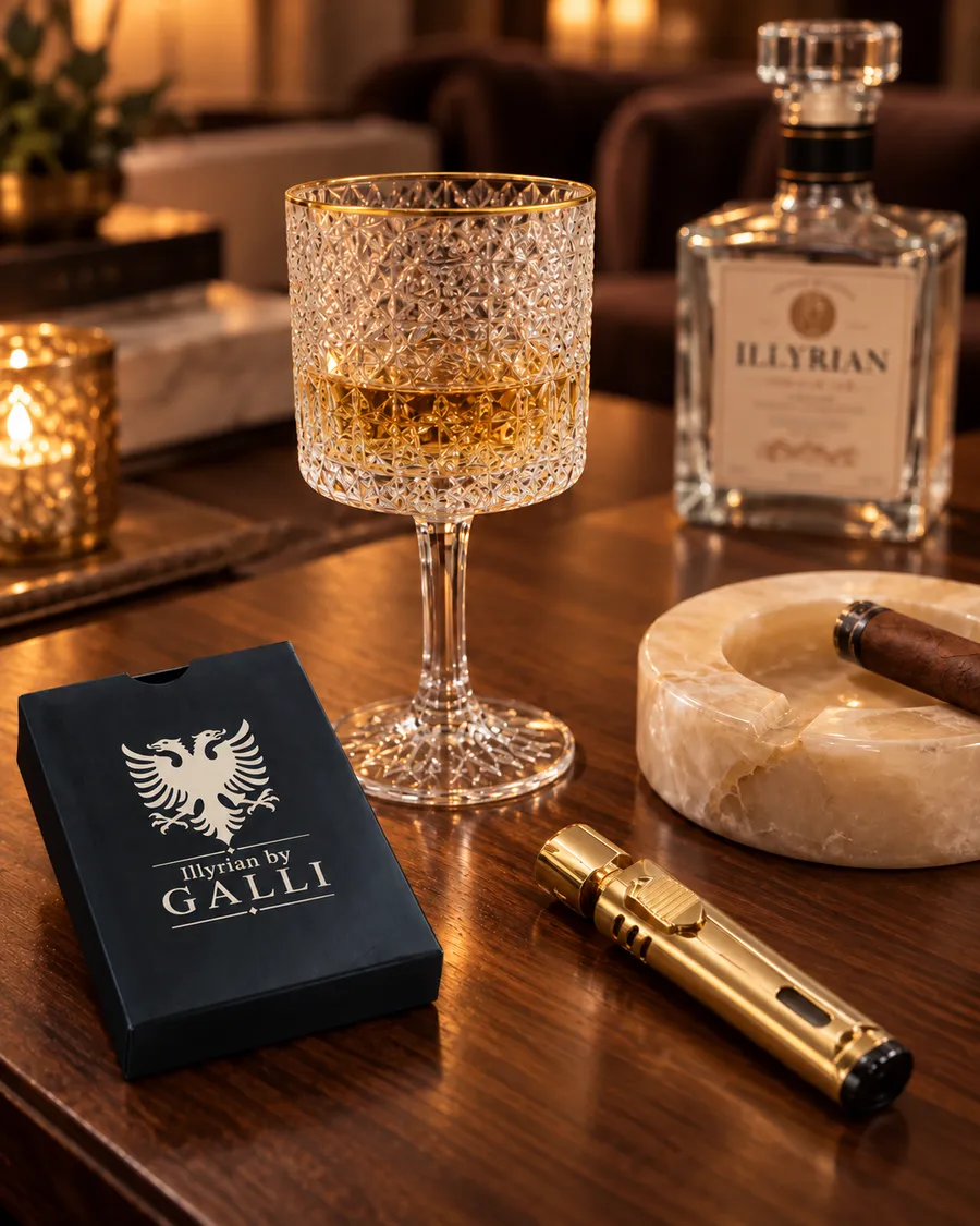 Evening salon scene with an Illyrian gin bottle, cut-crystal glasses, a gold lighter, Illyrian by Galli playing cards and a marble ashtray on a wooden table